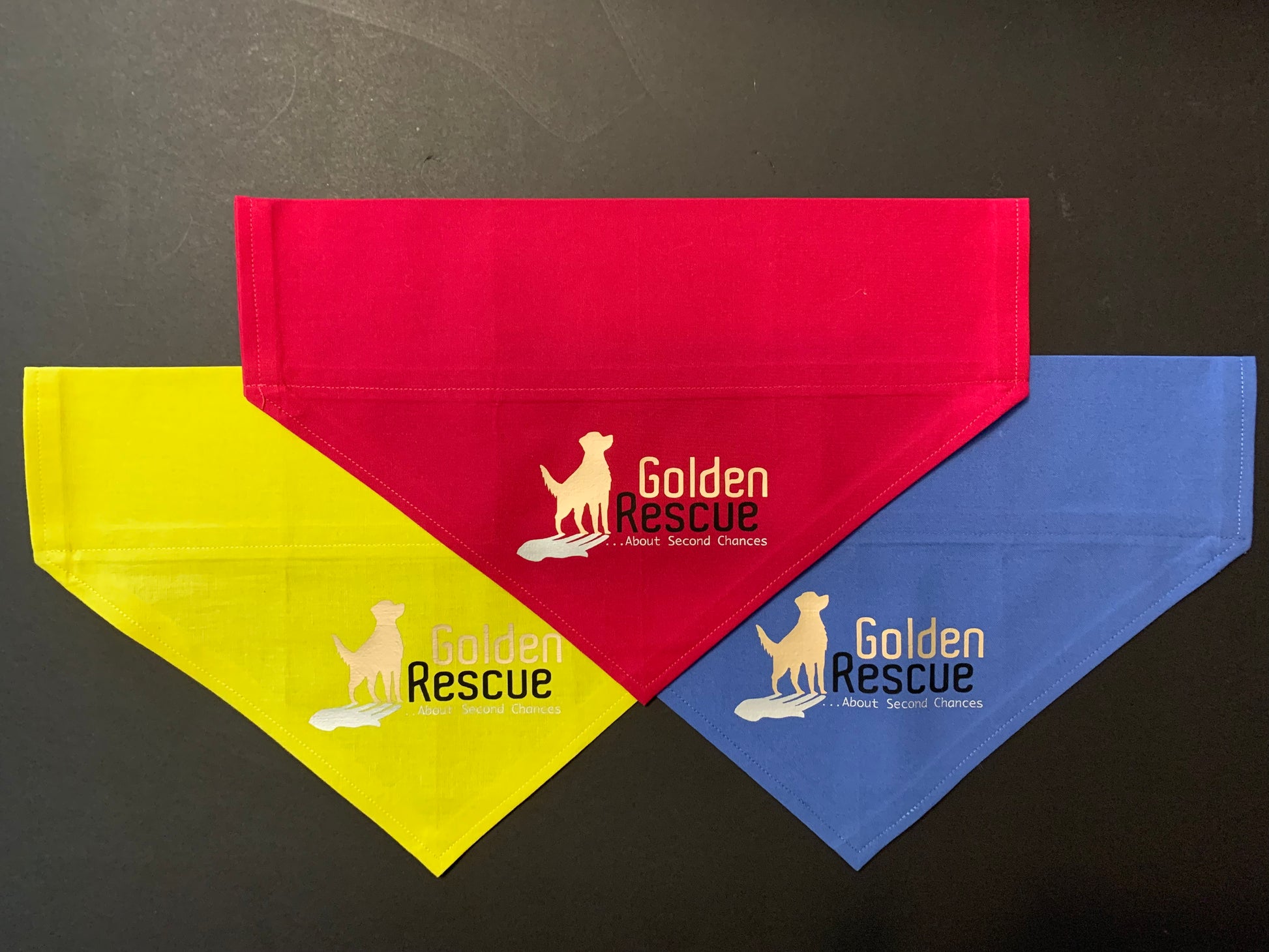 Three folded bandanas in red, blue, and yellow, each with the 'Golden Rescue' text and logo printed on the front.